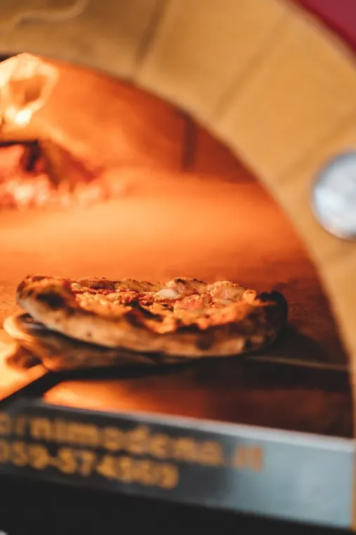 Una pizza dentro il forno a legna, illuminata dalla fiamma