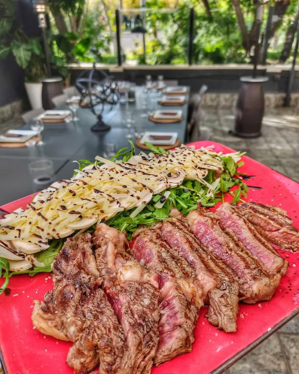 Tagliata di manzo affettata accanto a verdure grigliate su un tagliere rosso